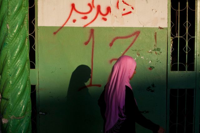 Une jeune femme passe devant un graffiti annonçant le début de la révolution (Lybis, 2012)