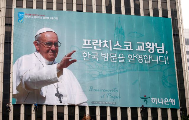 Les ouvriers installent une banderole géante représentant le pape et un message de bienvenue