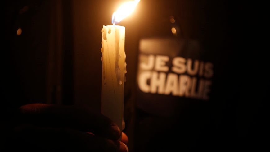 A person holds a candle in front a placard which reads "I am Charlie".