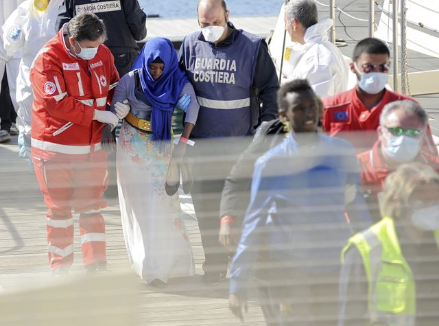 Une migrante est aidée à débarquer d'un bateau de la Garde côtière dans le port de Palerme