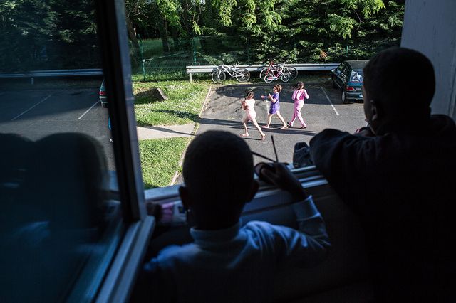 Deux frères d'origine érythréenne observent d'autres enfants jouer dehors avec envie.