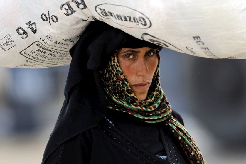 A Syrian refugee woman carries her belongings as she crosses into Turkey at Akcakale border gate in Sanliurfa...
