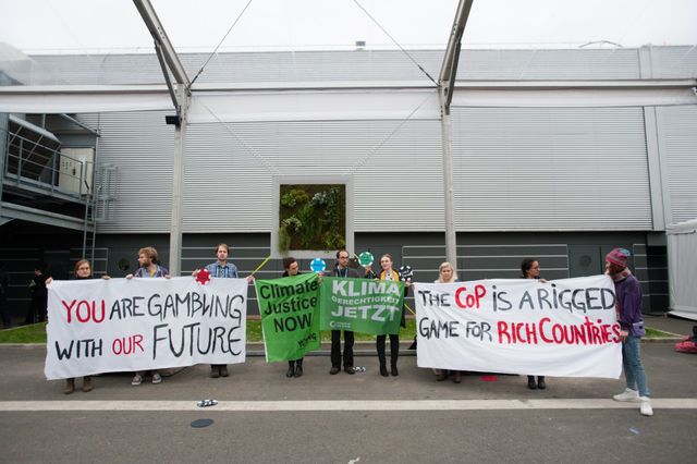 Des manifestants à l'intérieur de la COP21. Sur les panneaux, on lit : « Un jeu truqué pour les pays riches »