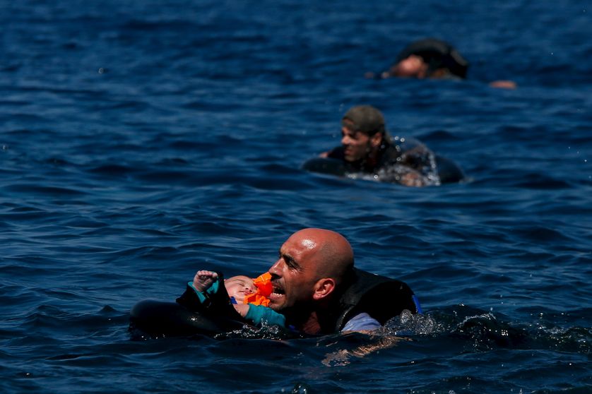 A Syrian refugee holding a baby in a lifetube swims towards the shore after their dinghy deflated some...