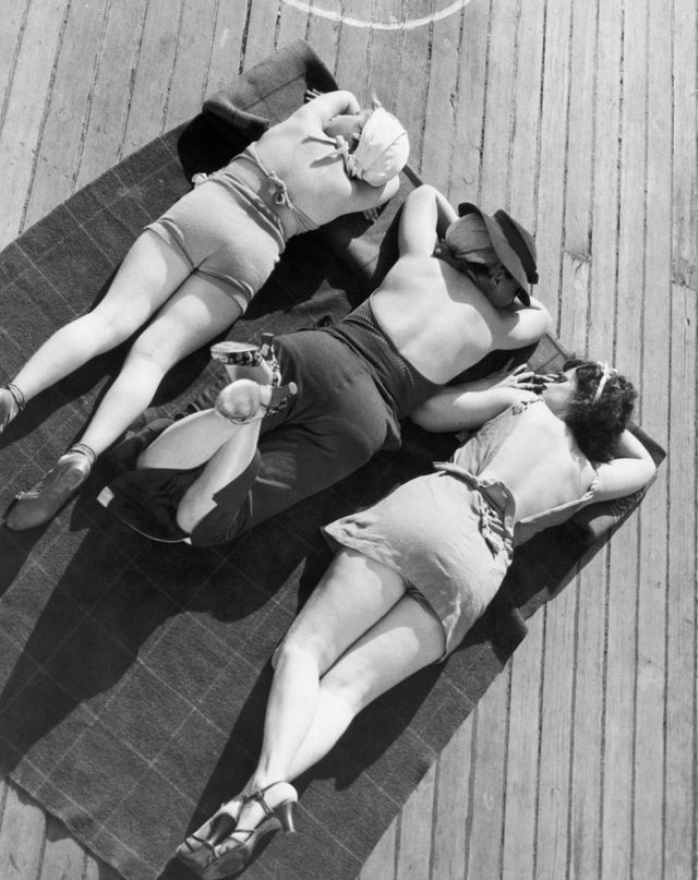 Trois baigneurs sur une serviette sur le pont du navire (ca. 1930 - 1959)