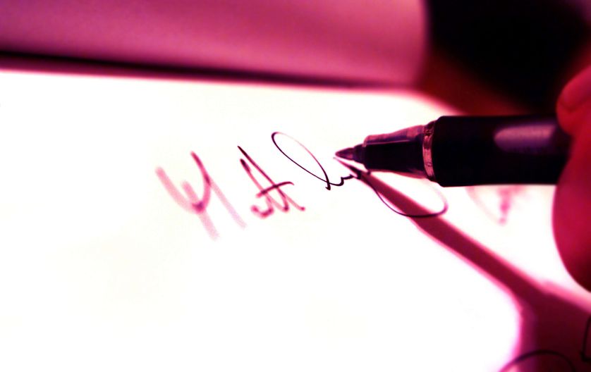 Someone writing signature with a pen and white paper