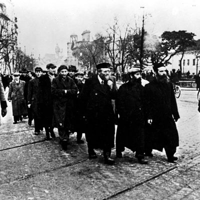 Varsovie, 1940. Groupe de juifs marchant dans les rues escortés et surveillés par des soldats SS de l'armée allemande occupant le pays.