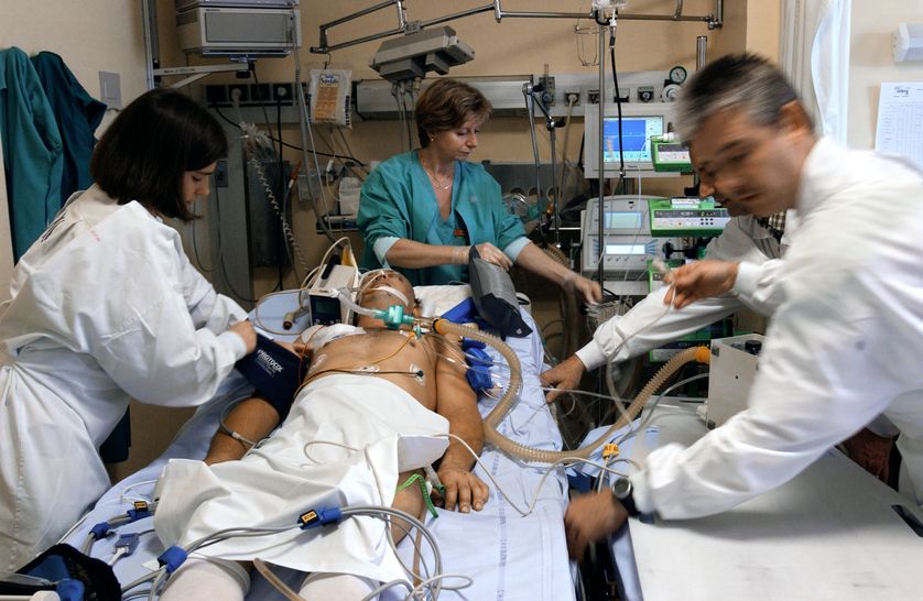 Un médecin assité d'une externe, d'une infirmière et d'un brancardier se préparent à transférer un malade dans le coma du service de réanimation vers la radiologie pour passer un scanner