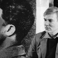 Portrait de l'artiste américain Andy Warhol posant devant une de ses sérigraphies dans son atelier de la Factory en 1966.