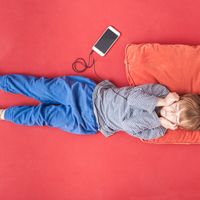 Little boy lying on bed hearing music with smartphone and earphones