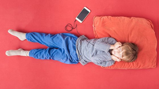 Little boy lying on bed hearing music with smartphone and earphones ©Getty - Westend61