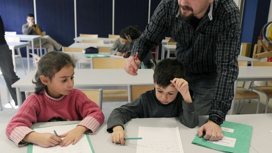 Un maître d'école corrige les exercices d'écriture d'un petit groupe d'écoliers du cours préparatoire (CP) dans une école de la banlieue de Saint Etienne, 29/11/2010 ©AFP - PHILIPPE DESMAZES / AFP