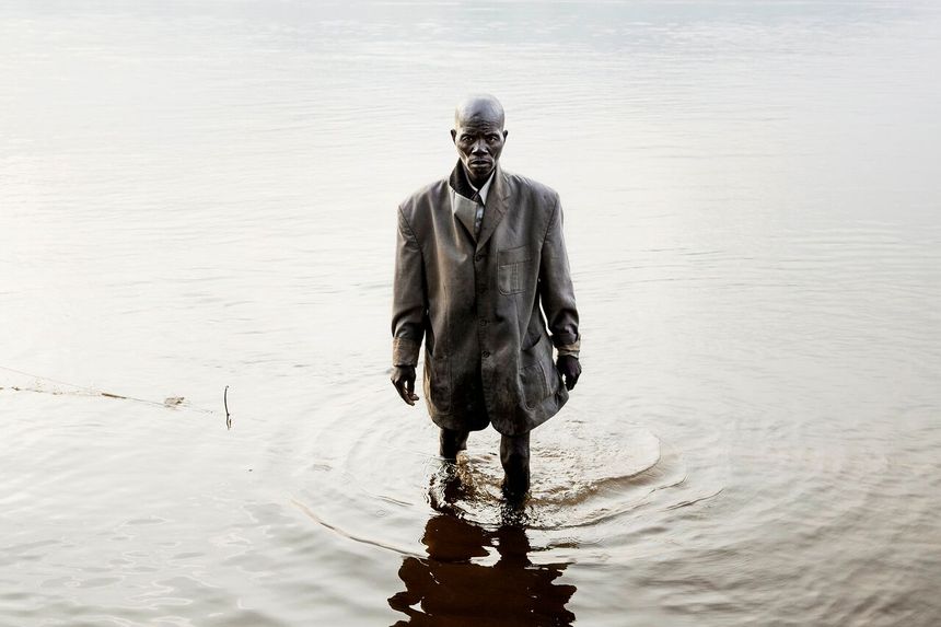 Un pêcheur habillé pour la messe dominicale marche dans la rivière Oubangui, tôt le matin