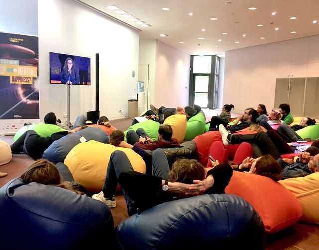 Les curieux qui n’ont pas eu de places dans l’auditorium se retrouvent par dizaines sur des poufs devant un écran qui retransmet les conférences.