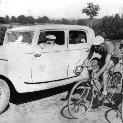 L'écrivain Tristan Bernard dans l'automobile, souriant aux coureurs du tours de France en 1936, durant l'étape Bordeaux-La Rochelle