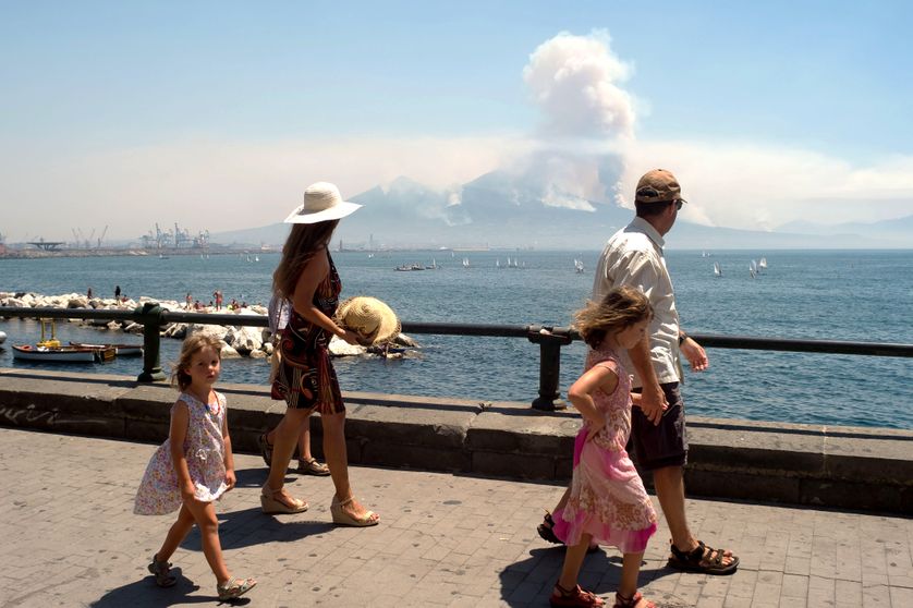 Sur la promenade de Naples, des passants regardent au loin la fumée s'échapper du Vésuve
