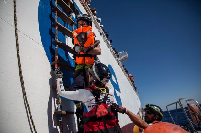 Un sauveteur de l'Aquarius tient une petite fille récupérée avec d'autres personnes depuis le navire marchand Santa Lucia en Méditerranée, à 20 milles nautiques de la côte libyenne. / AFP