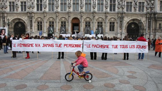 Une fillette passe en vélo devant une banderole déployée sur le parvis de l'Hôtel de Ville de Paris lors d'un rassemblement, regroupant des personnalités du monde du spectacle et d'associations, contre les violences faites aux femmes.(28/10/2007) ©AFP - PATRICK KOVARIK / AFP