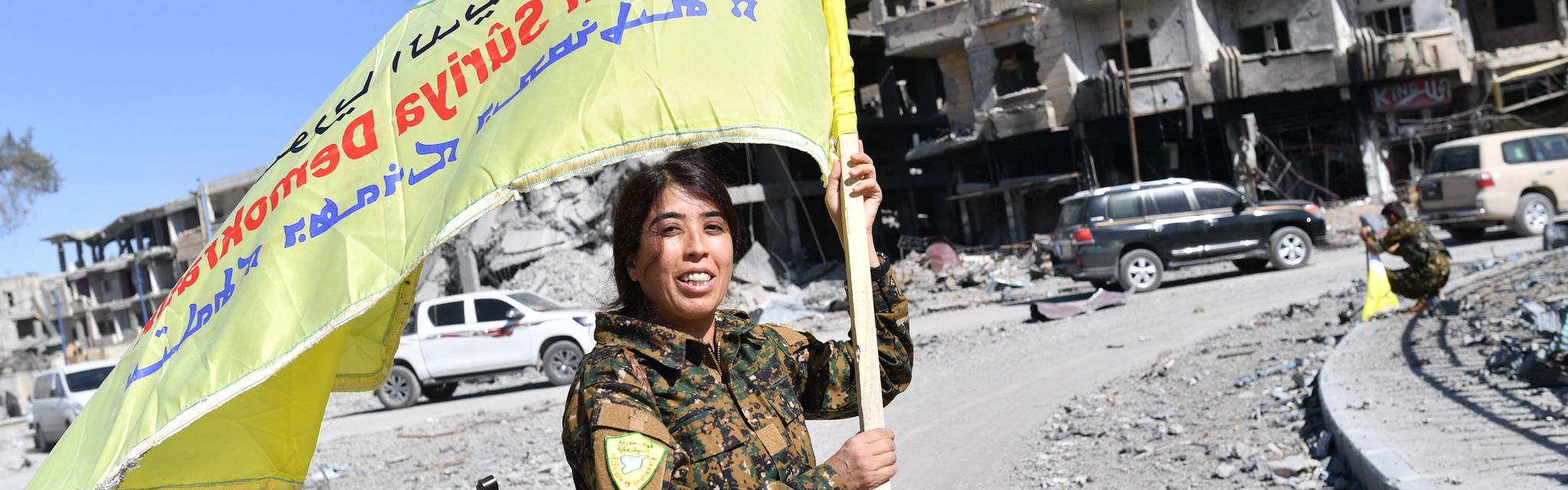 Une combattante kurde brandit le drapeau des FDS dans les rues dévastées de Raqqa