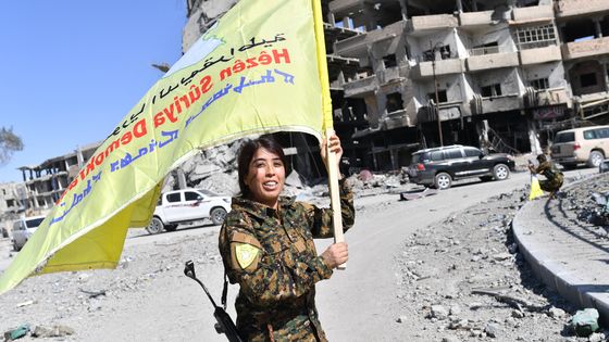 Une combattante kurde brandit le drapeau des FDS dans les rues dévastées de Raqqa ©AFP - BULENT KILIC