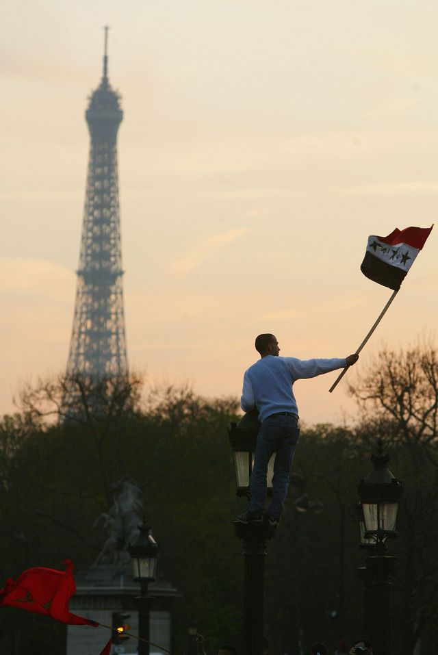 Perché sur un lampadaire, un manifestant agite un drapeau irakien lors d'un rassemblement condamnant l'action militaire contre l'Irak menée par les forces de la coalition (place de la Concorde à Paris, le 20 mars 2003)