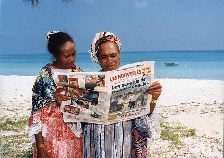 Deux femmes lisent le journal sur une plage de Nouvelle Calédonie suite à la signature de l'Accord de Nouméa, avril 1998