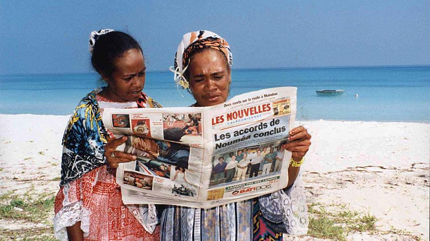 Deux femmes lisent le journal sur une plage de Nouvelle Calédonie suite à la signature de l'Accord de Nouméa, avril 1998