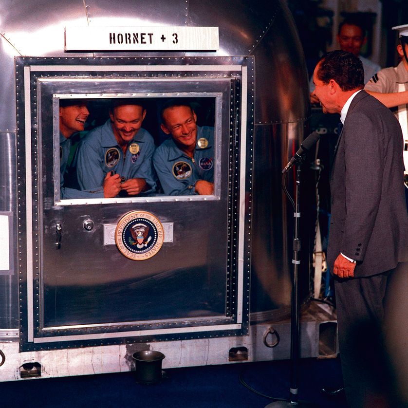 Neil A. Armstrong, Michael Collins, et Edwin E. Aldrin, Jr., sont en quarantaine après leur mission réussie sur la Lune en juillet 69, souriants au Président Nixon.
