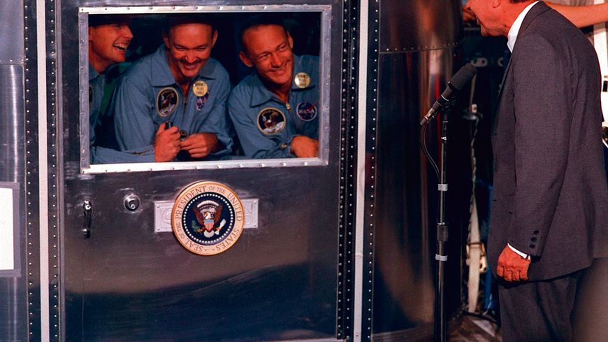 Neil A. Armstrong, Michael Collins, et Edwin E. Aldrin, Jr., sont en quarantaine après leur mission réussie sur la Lune en juillet 69, souriants au Président Nixon.