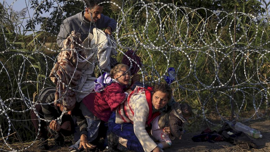 Syrian migrants cross under a fence as they enter Hungary at the border with Serbia