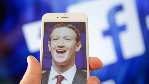 Un portrait du PDG de Facebook Mark Zuckerberg, sur un écran d'iPhone, devant le logo du réseau social Facebook ©AFP - Jaap Arriens / NurPhoto