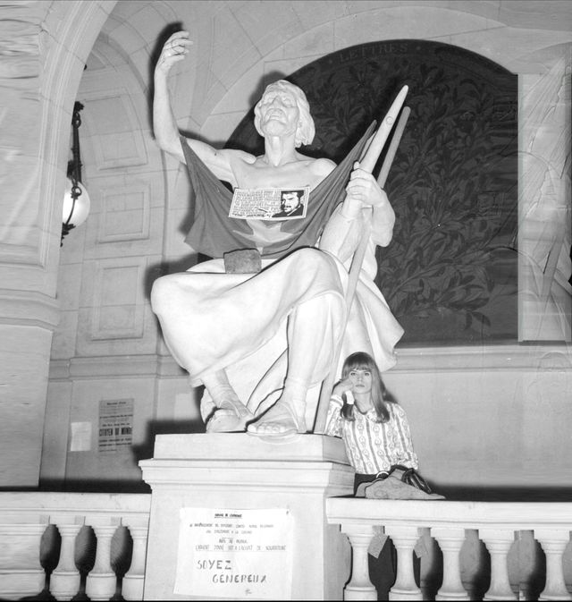 Une jeune étudiante se repose dans le hall d'entrée de la Sorbonne, le 21 mai 1968 à Paris, au pied d'une statue sur laquelle le drapeau chinois, une photo et une citation du révolutionnaire cubain Che Guevara ont été accrochés, lors d'une réunion d'