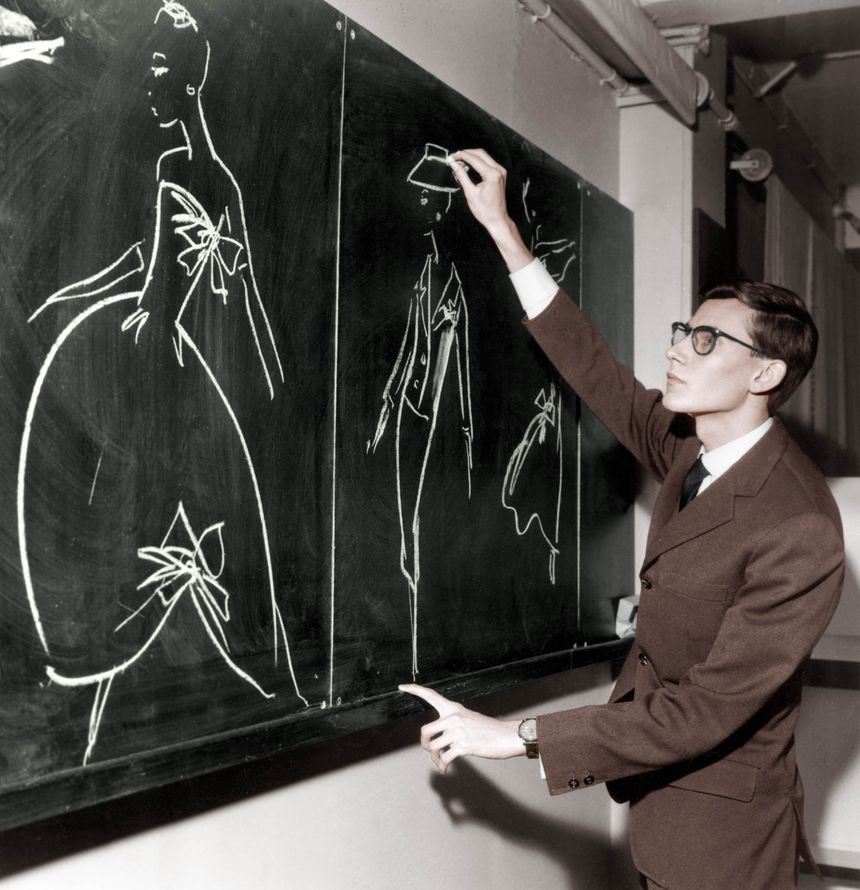 Yves Saint Laurent dessinant des modèles sur un tableau, en novembre 1957. (Photo colorisée)