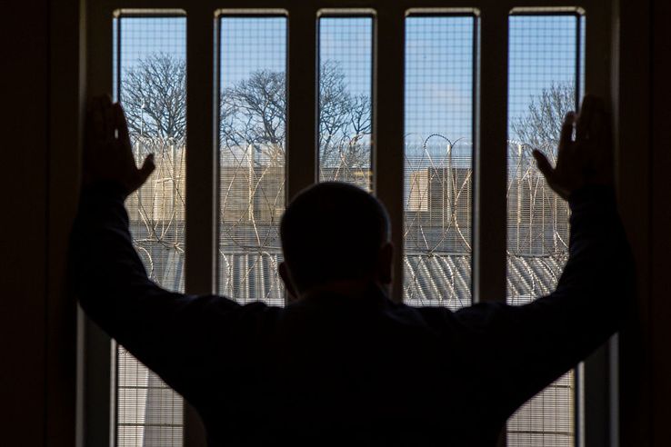 Un prisonnier regardant l'extérieur à travers une vitre renforcée.