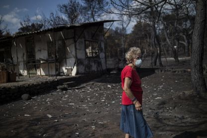 Une femme portant un masque marche devant sa maison brûlée suite à un incendie de forêt dans le village de Neos Voutzas, près d'Athènes, le 26 juillet 2018. Une femme portant un masque marche devant sa maison brûlée suite à un incendie de forêt dans le village de Neos Voutzas, près d'Athènes, le 26 juillet 2018.