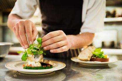 Gros plan d'un Chef dans sa cuisine ajoutant une garniture de salade à une assiette de poisson grillé. Gros plan d'un Chef dans sa cuisine ajoutant une garniture de salade à une assiette de poisson grillé.