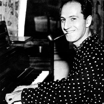 Profile headshot of American composer George Gershwin (1898 - 1937) writing notes on a musical score while sitting at his piano, New York City
