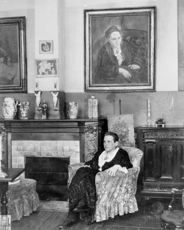 Gertrude Stein photographiée chez elle, sous le portrait que Picasso lui a dédié (1906) au 27 rue de Fleurus dans le 6ème arrondissement de Paris.