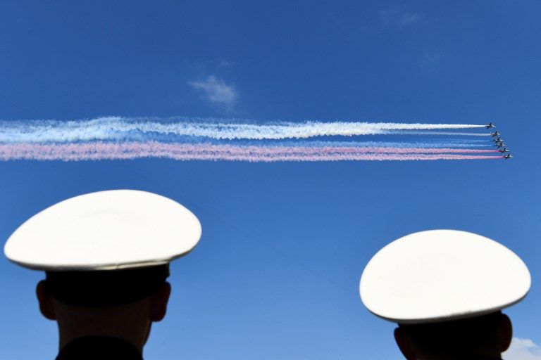 Des avions d’assaut russes libèrent de la fumée aux couleurs du drapeau russe alors qu’ils survolent la Neva, lors du défilé du Jour de la Marine à Saint-Pétersbourg le 29 juillet 2018.