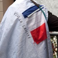 Un homme avec un drapeau français et une inscription 'Vive la laïcité' se recueille devant la plaque commémorative en mémoire des victimes des attentats du 13 novembre 2015 devant le Bataclan