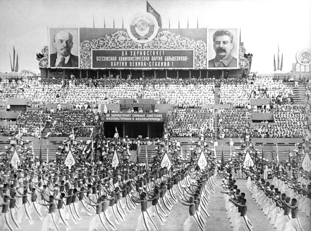 Les gymnastes soviétiques portant des drapeaux avec le marteau et la faucille défilent sous les portraits de Lénine et de Staline à l'occasion de la fête des Sports à Moscou au mois d'août 1946.