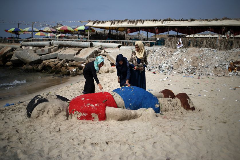 De jeunes Palestiniennes déposent des fleurs sur une sculpture représentant le corps d'Aylan, sur une plage de Gaza.