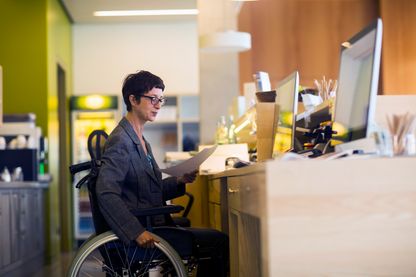 Femme en fauteuil roulant, au travail dans un bureau Femme en fauteuil roulant, au travail dans un bureau