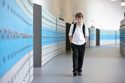Unhappy schoolboy walking alone in school corridor Unhappy schoolboy walking alone in school corridor
