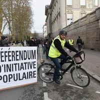 Manifestant sur un vélo transportant une pancarte en faveur du RIC, Référendum d’Initiative Citoyenne.