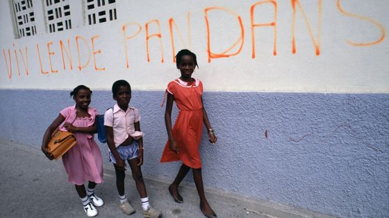 Trois enfants guadeloupéens vont à l'école en passant devant un mur sur lequel est écrit 'Vive l'indépendance' à Pointe-à-Pitre, France. ©Getty - JEAN-LUC MANAUD/Gamma-Rapho