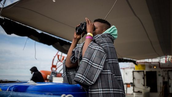 Depuis le bateau de sauvetage néerlandais Sea Watch 3, un mineur non accompagné regarde la côte italienne à travers des jumelles. ©AFP - FEDERICO SCOPPA