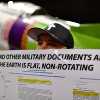 Novembre 2018, T. John brandissant une pancarte "la Nasa et d'autres documents militaires admettent que la Terre est plate, et non ronde" à la conférence Terre Plate Internationale, à Denver.