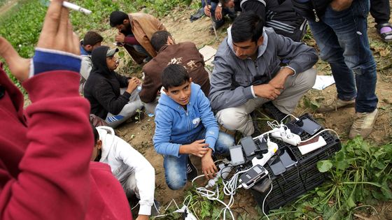 Des migrants chargent leurs smartphones alors qu'ils attendent à quelques mètres de la frontière croate, après avoir parcouru les derniers kilomètres entre Serbie et Croatie à Sid, en Serbie (2015). ©Getty - Carsten Koall