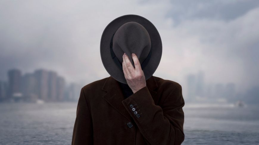 Un homme cachant son visage avec son chapeau à NY.
